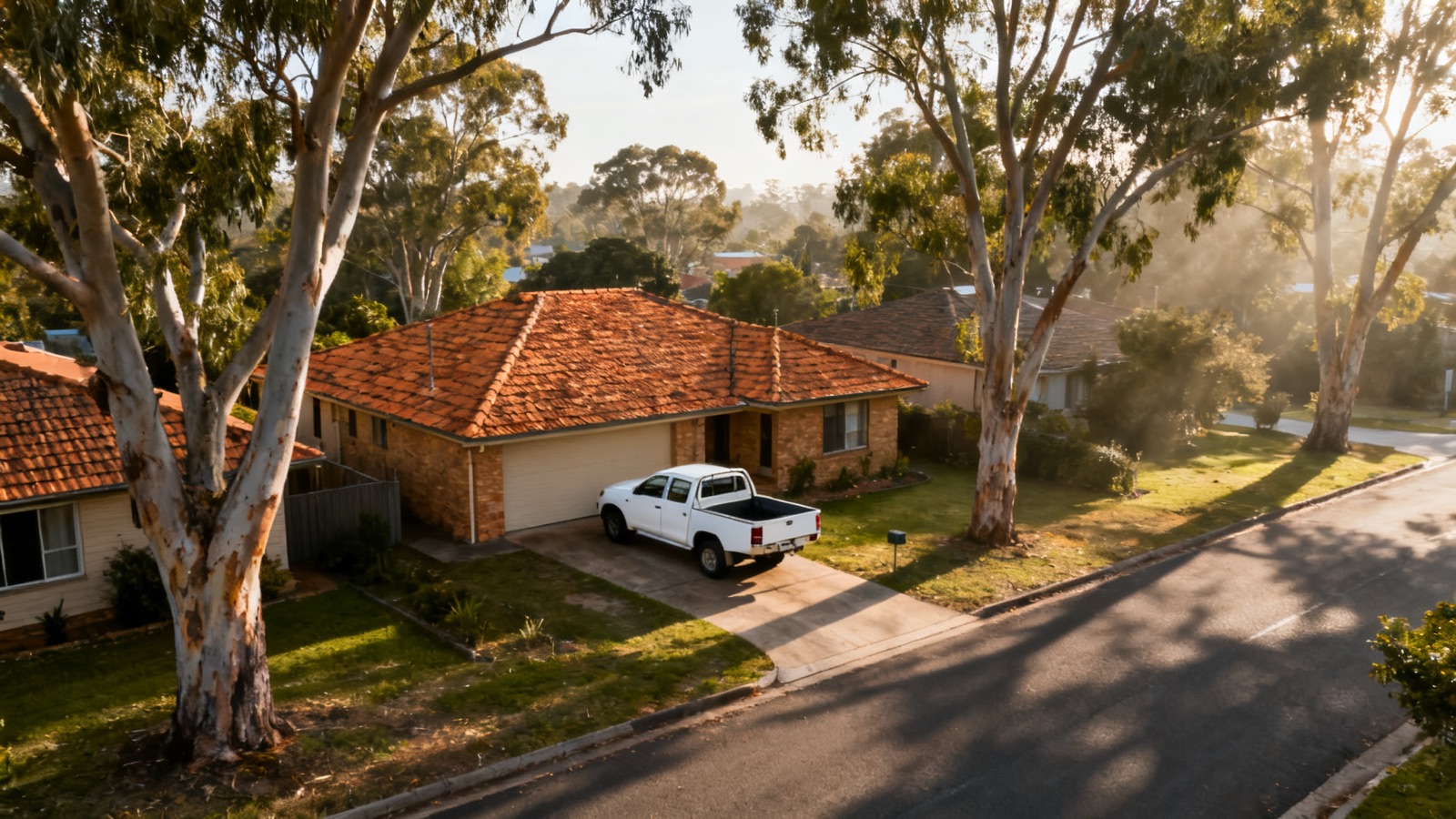Aerial view of an Australian suburban street with terracotta tile roofs and a parked ute